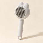 Gray pet massage and deshedding comb on a warm ivory background.